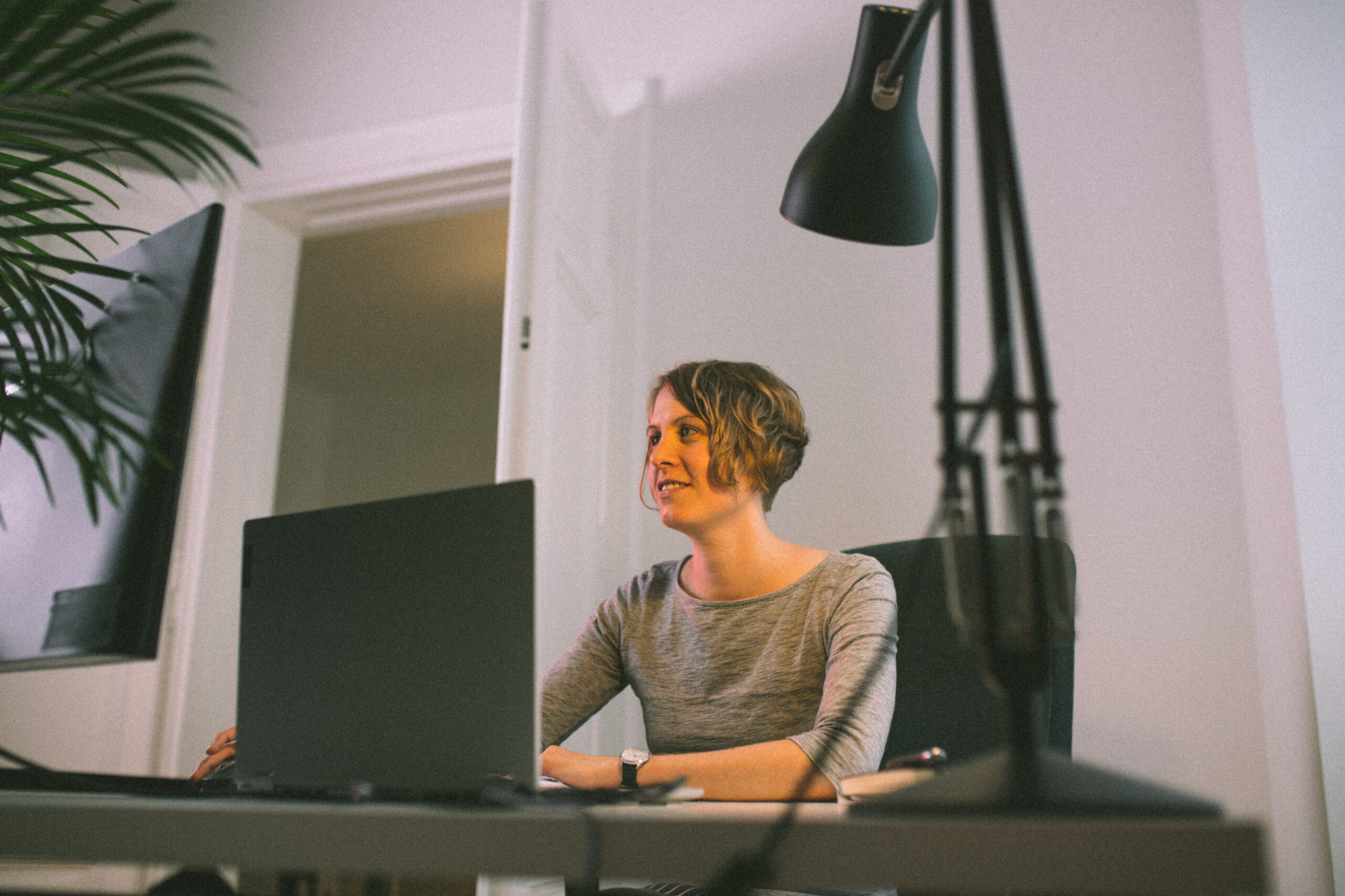 Sabine sitting at workplace with laptop, lamp and plant
